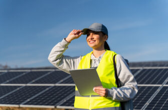 Female energy specialist looking away with happy smile after using digital tablet for reading information to check the efficiency of solar panel construction. Green energy jobs, technology and innovation concept